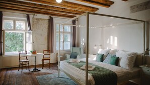 A four-poster bed with white linens, a green checkered bedspread, and multiple pillows. There is a small round table with chairs and a basket of fruit. The room has wooden floors and a window with curtains. - Miss Sophie's Olomouc (Olomouc)