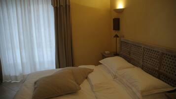 Una habitación de hotel con cama, cortinas, mesita de noche, lámpara y cabecero.