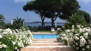 Zona de piscina con vista al mar, rodeada de flores blancas y árboles.