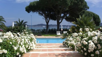 Zona de piscina con vista al mar, rodeada de flores blancas y árboles.
