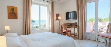 Habitación de hotel con cama, escritorio, silla, televisión y balcón con vistas.