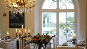 Mesa de comedor dispuesta con velas, un candelabro y una ventana con vistas a follaje.
