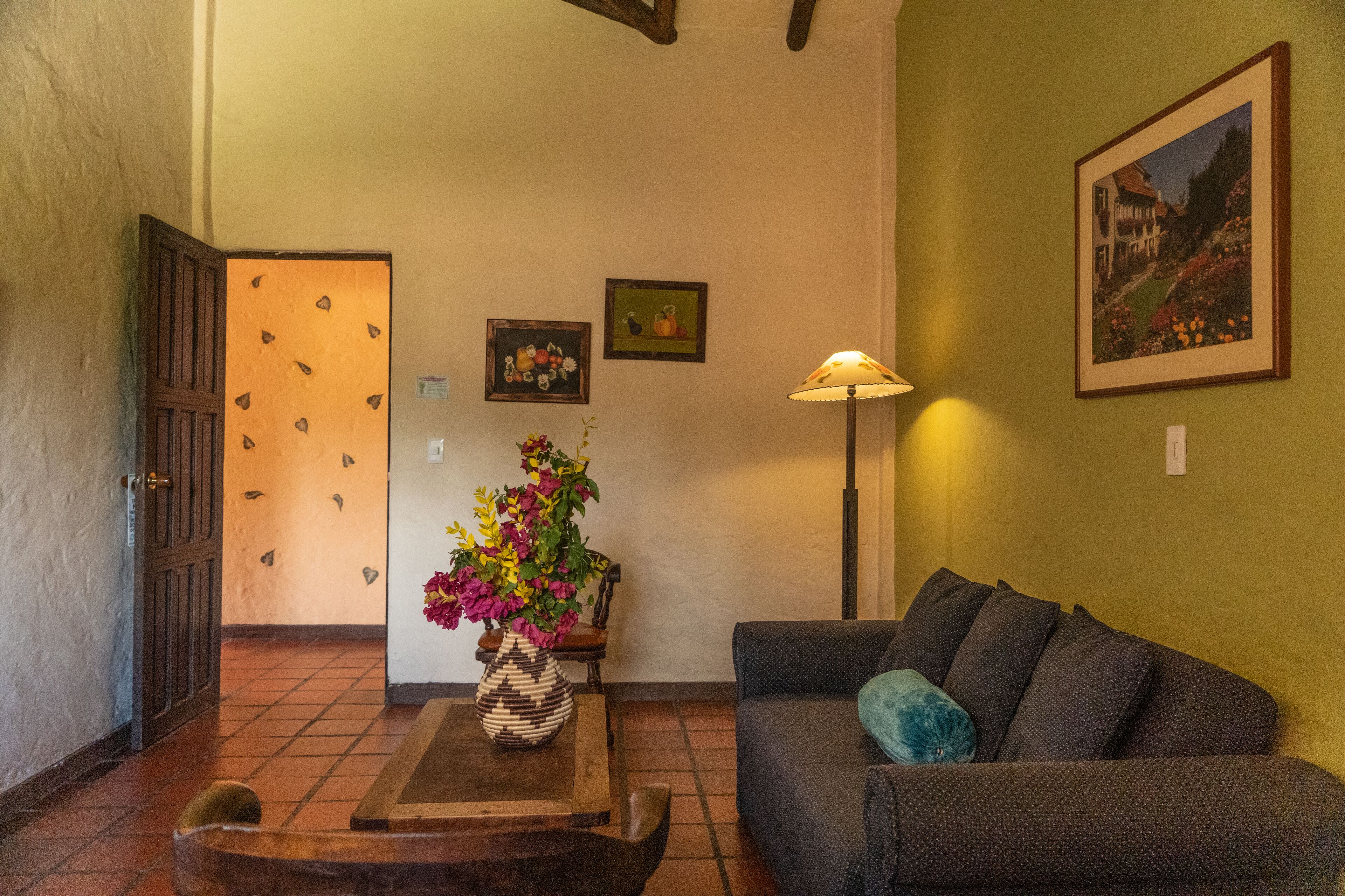 A cozy living room with a sofa, a coffee table with a vase of flowers, and a painting on the wall.