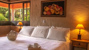 A neatly made bed with white linens, a bedside table with a lamp, and a basket of towels. - Hotel Termales El Batán (Cuitiva)