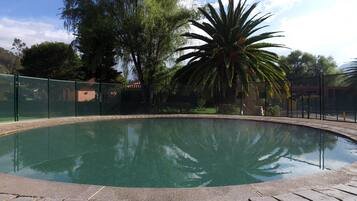 A swimming pool surrounded by a fence, with trees and a building in the background.