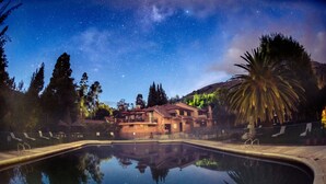 A swimming pool with a clear reflection of a building and trees, surrounded by a fence, under a starry night sky. - Hotel Termales El Batán (Cuitiva)