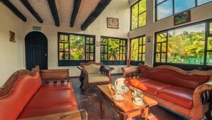 A room with wooden furniture, a black door labeled "SALIDA," and large windows with a view of greenery. - Hotel Termales El Batán (Cuitiva)