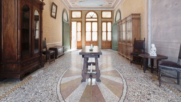 Uma sala imponente com uma mesa central, armários de madeira e um candelabro.