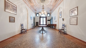 Um corredor com piso de pedra polida, teto ricamente decorado e obras de arte emolduradas nas paredes.