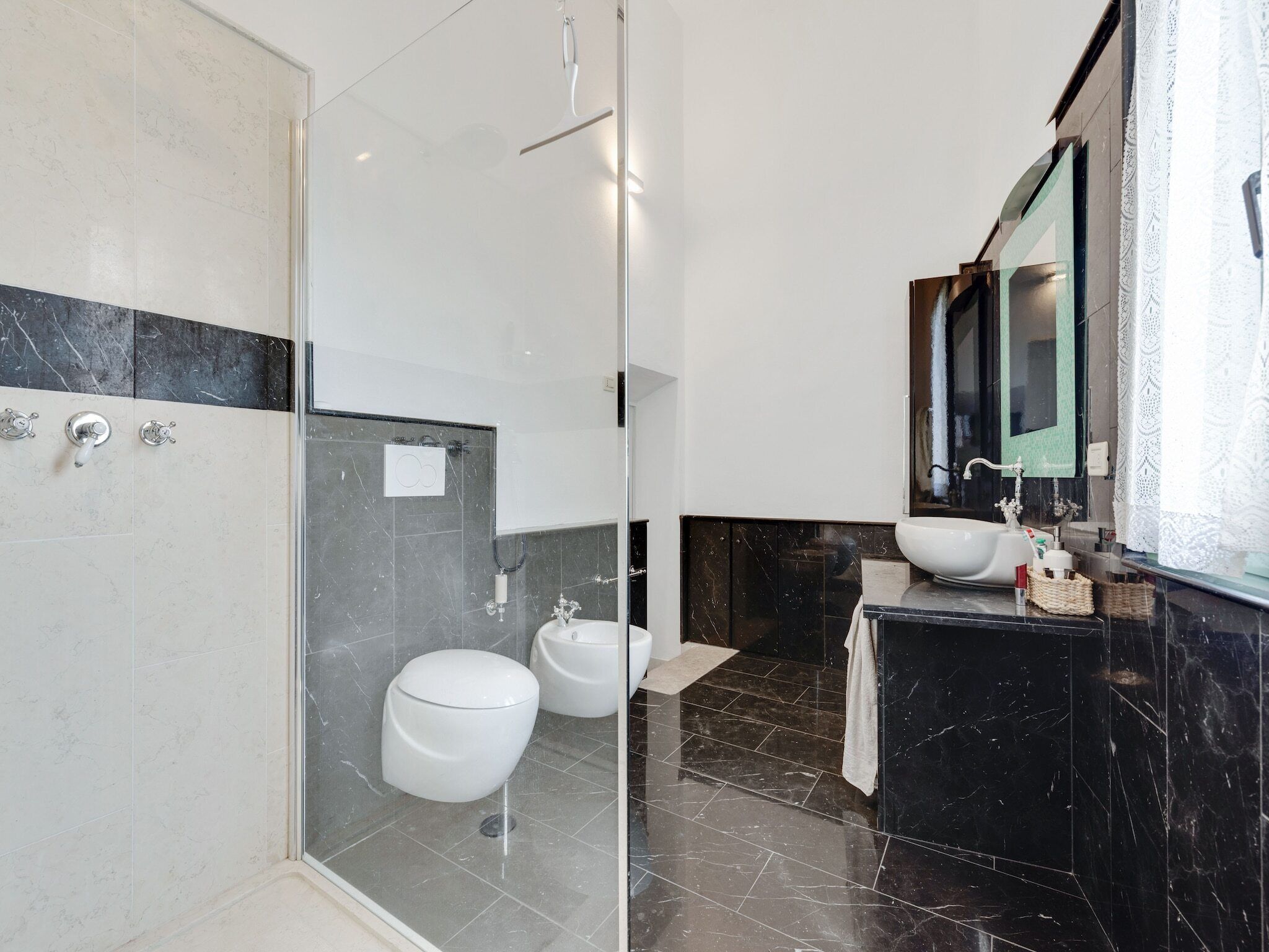 Un baño moderno con cabina de ducha de vidrio, dos inodoros, un lavamanos y un espejo.
