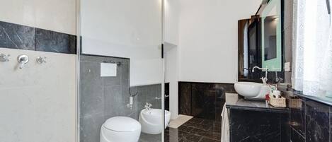 Un baño moderno con cabina de ducha de vidrio, dos inodoros, un lavamanos y un espejo.