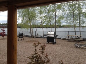 Ein überdachter Außenbereich mit Grill und Picknicktisch am See.