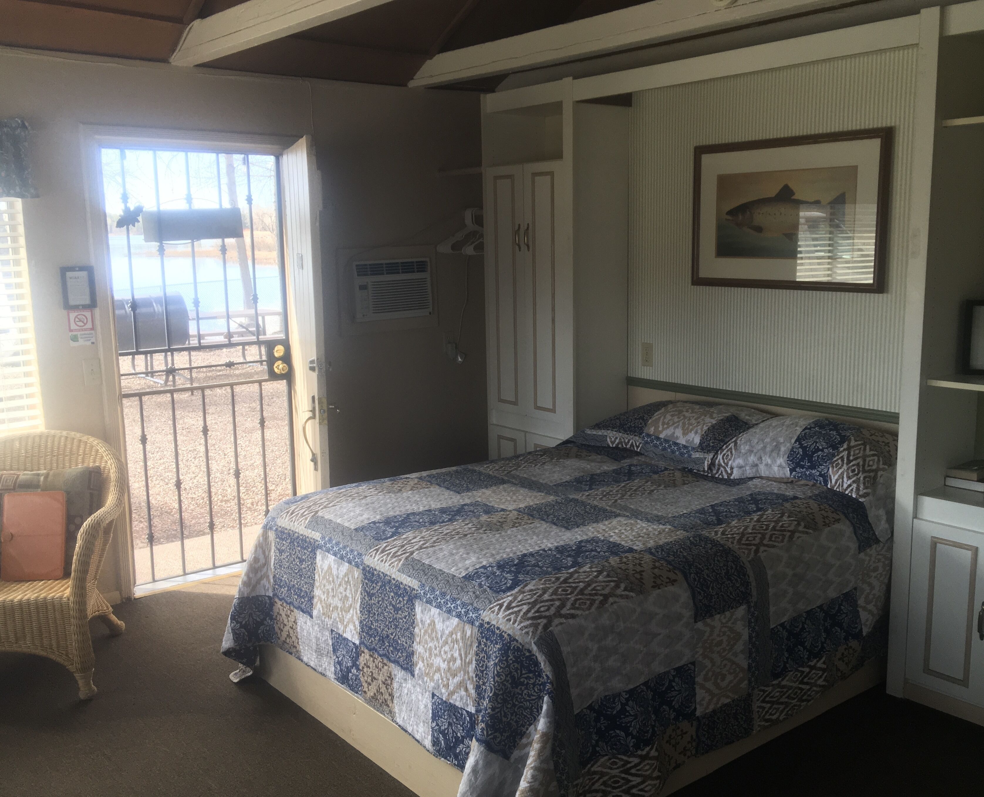A bedroom with a bed, a chair, a door leading to a balcony, and a framed picture on the wall.