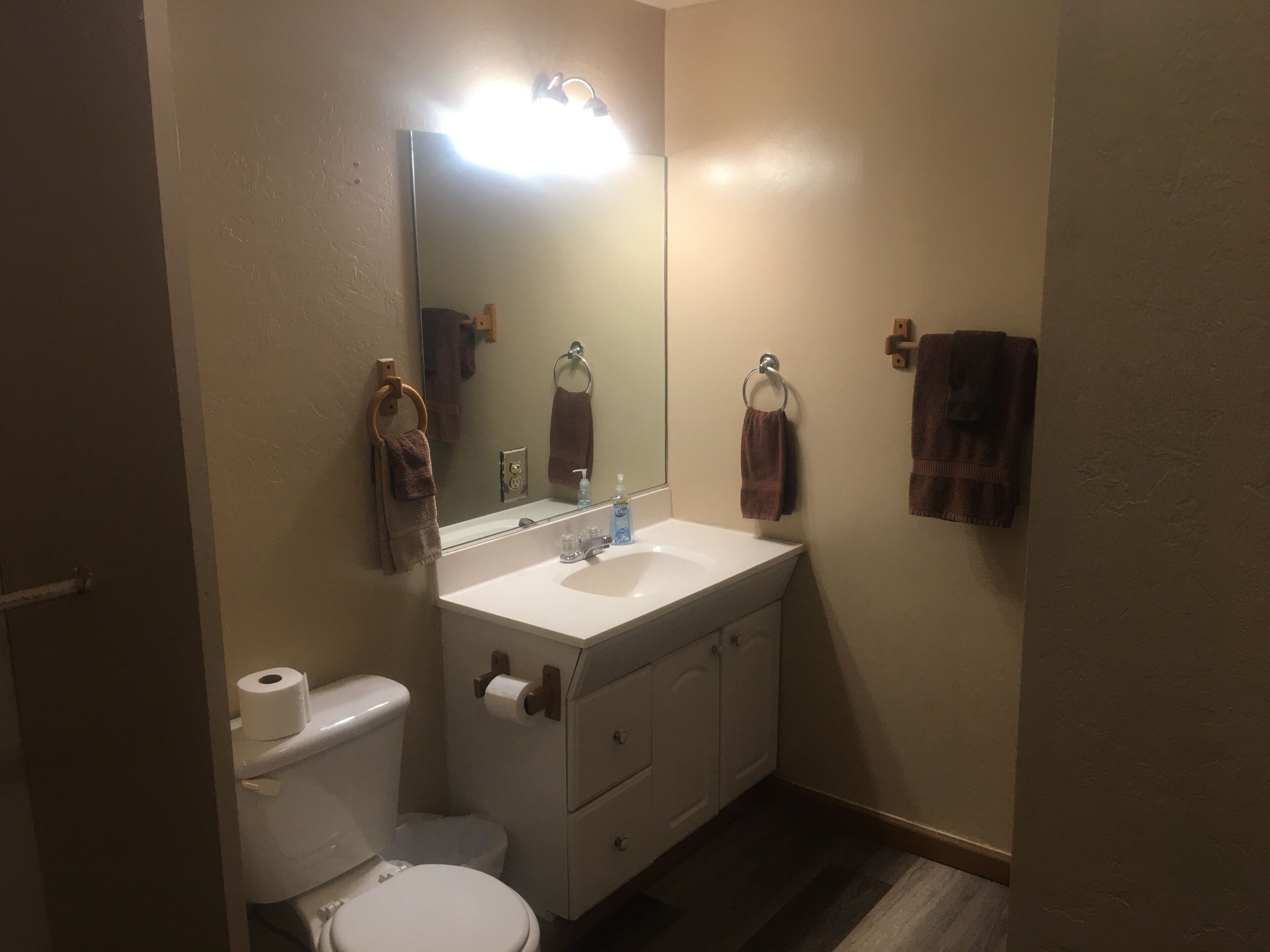 Un baño con inodoro, lavabo y espejo. Hay toallas colgadas en la pared y un rollo de papel higiénico en el inodoro.