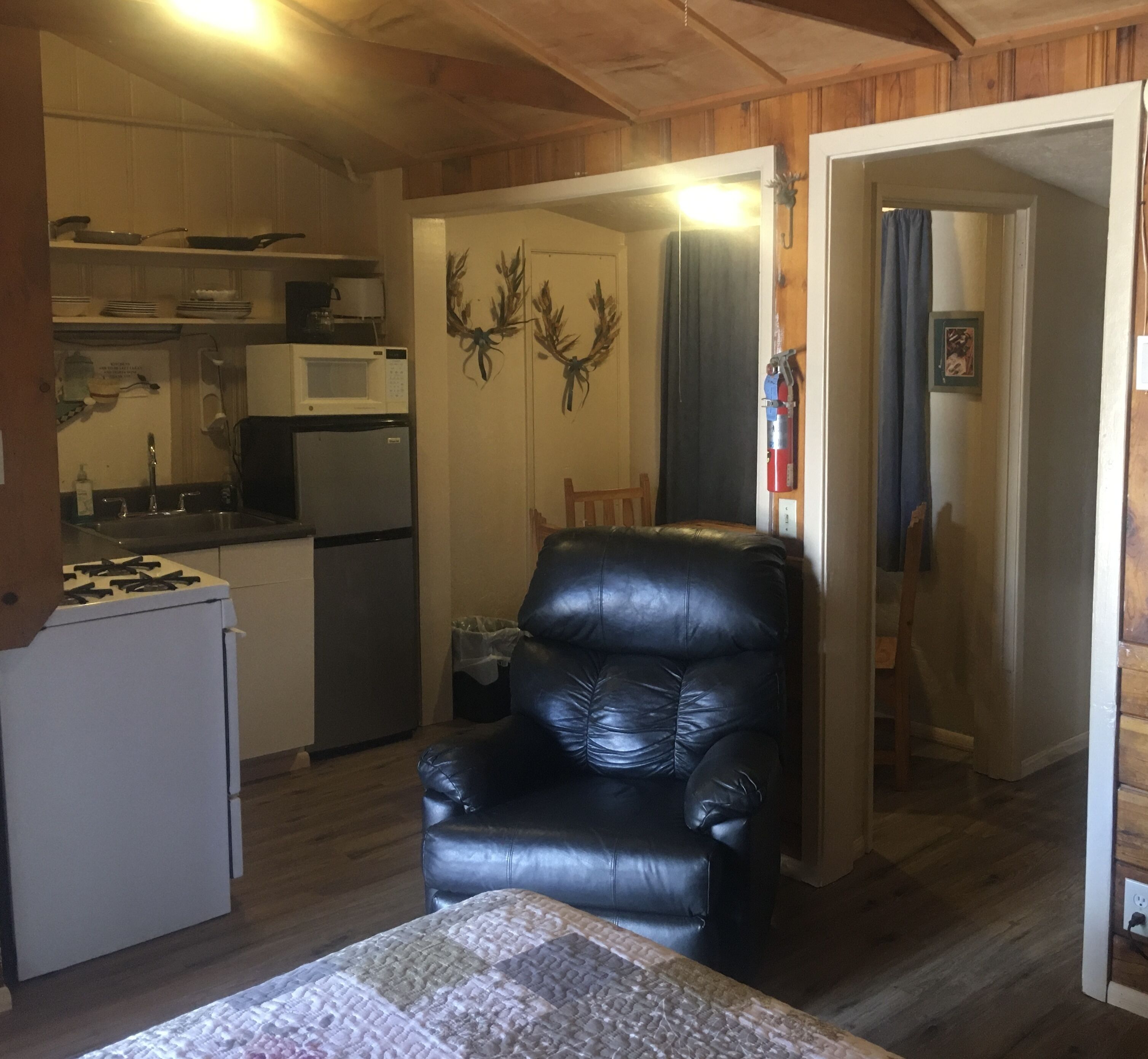 Eine kompakte Küche mit Kühlschrank, Mikrowelle und Herd. Ein schwarzer Ledersessel befindet sich im Wohnbereich.