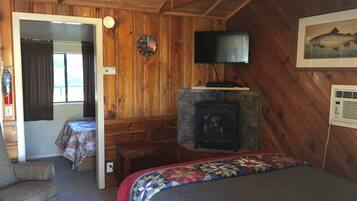 A cozy cabin room with a bed, a fireplace, a television, and a door leading to another room.