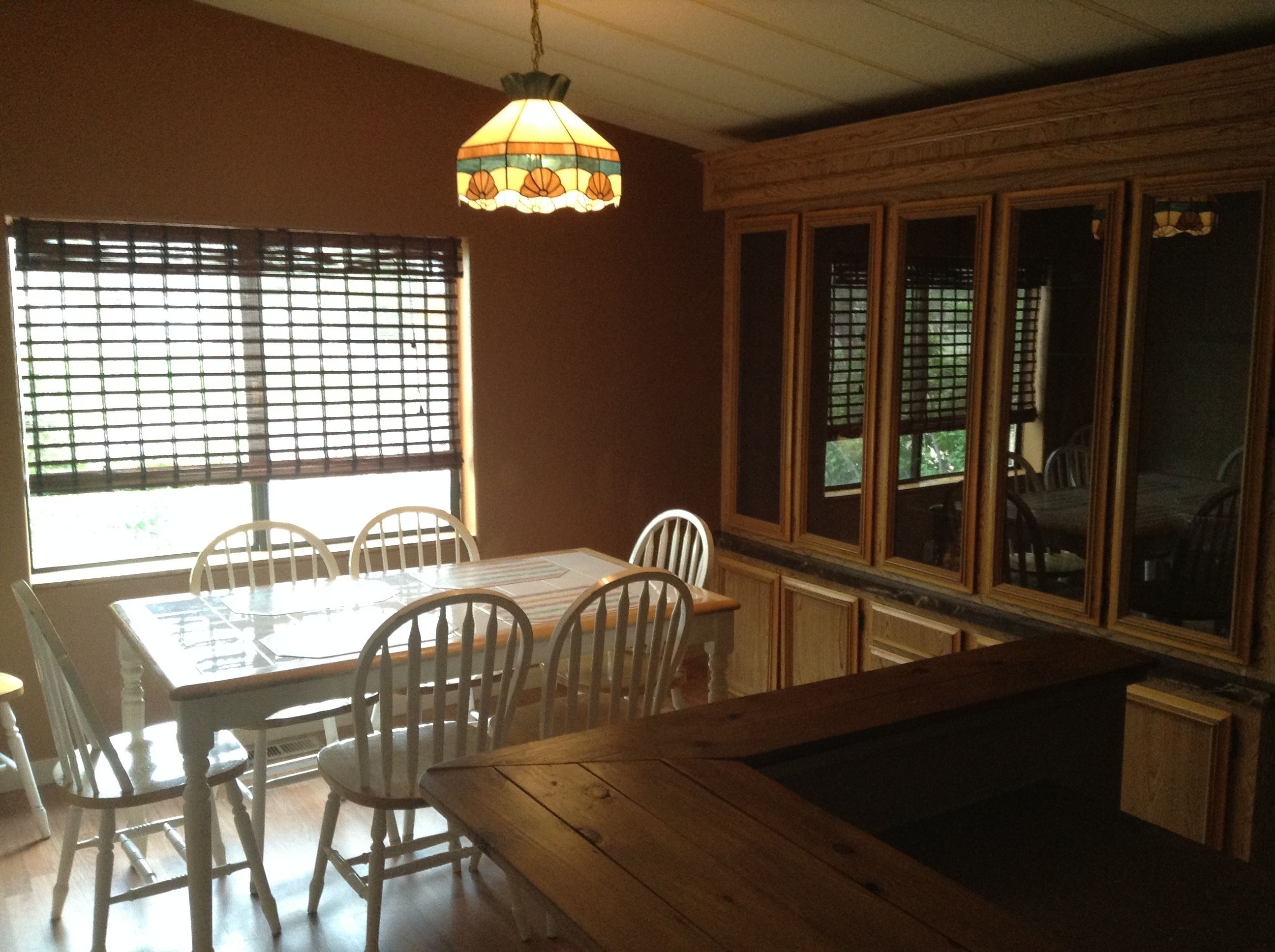A dining area with a wooden table and chairs, a hanging light fixture, and a window with blinds.