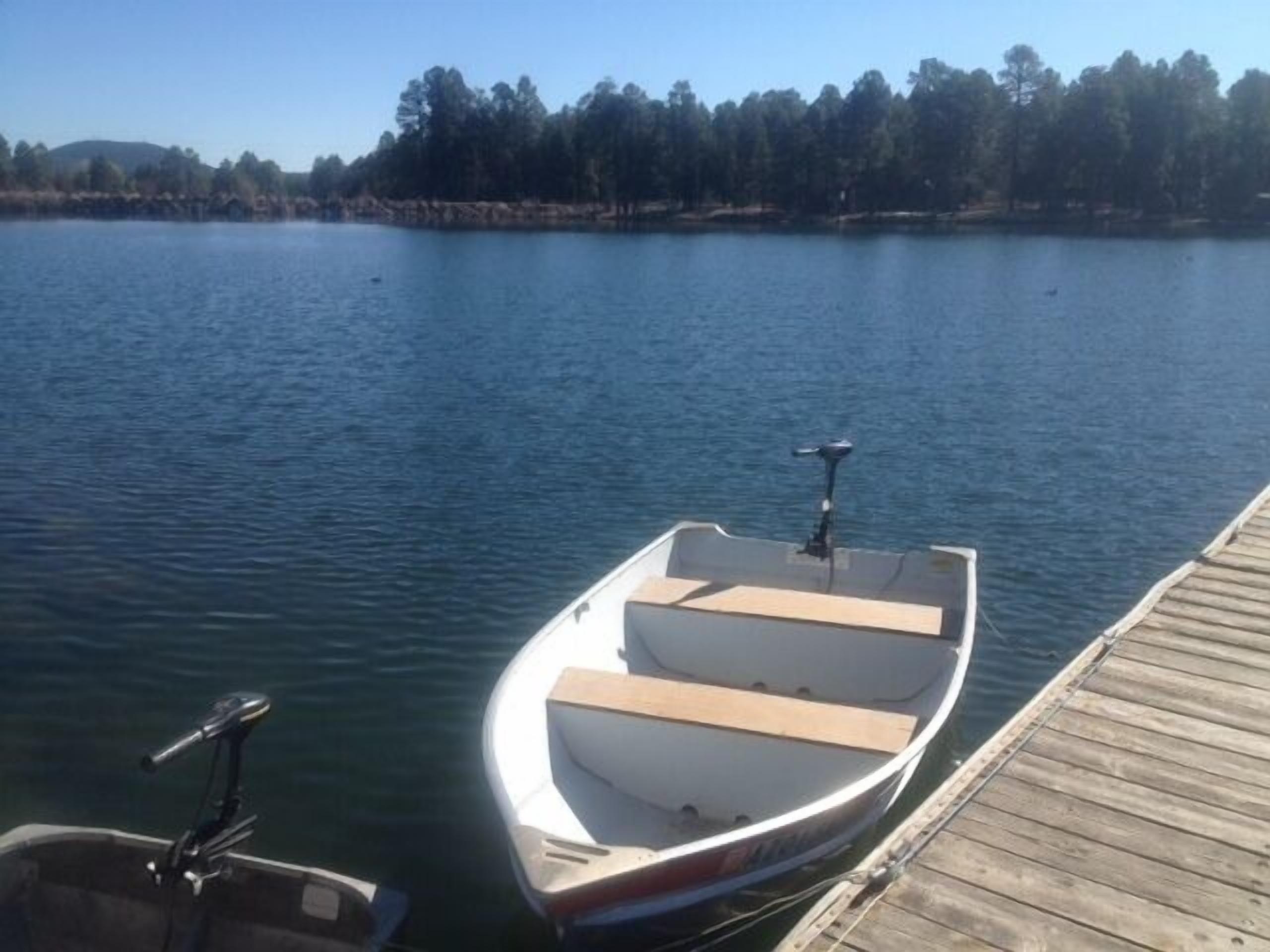 A small boat docked at a wooden pier, with calm water and a forested shoreline in the background.
