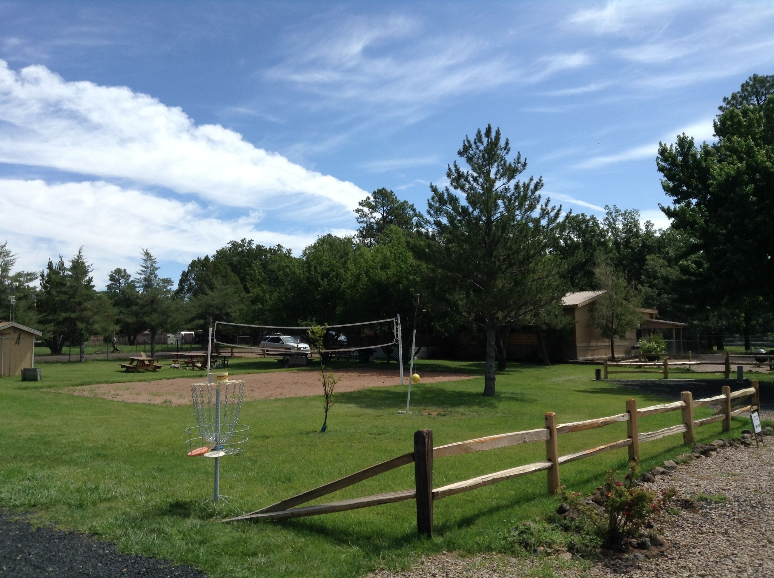 Um parque com uma rede de voleibol, mesas para piquenique e uma cerca de madeira.