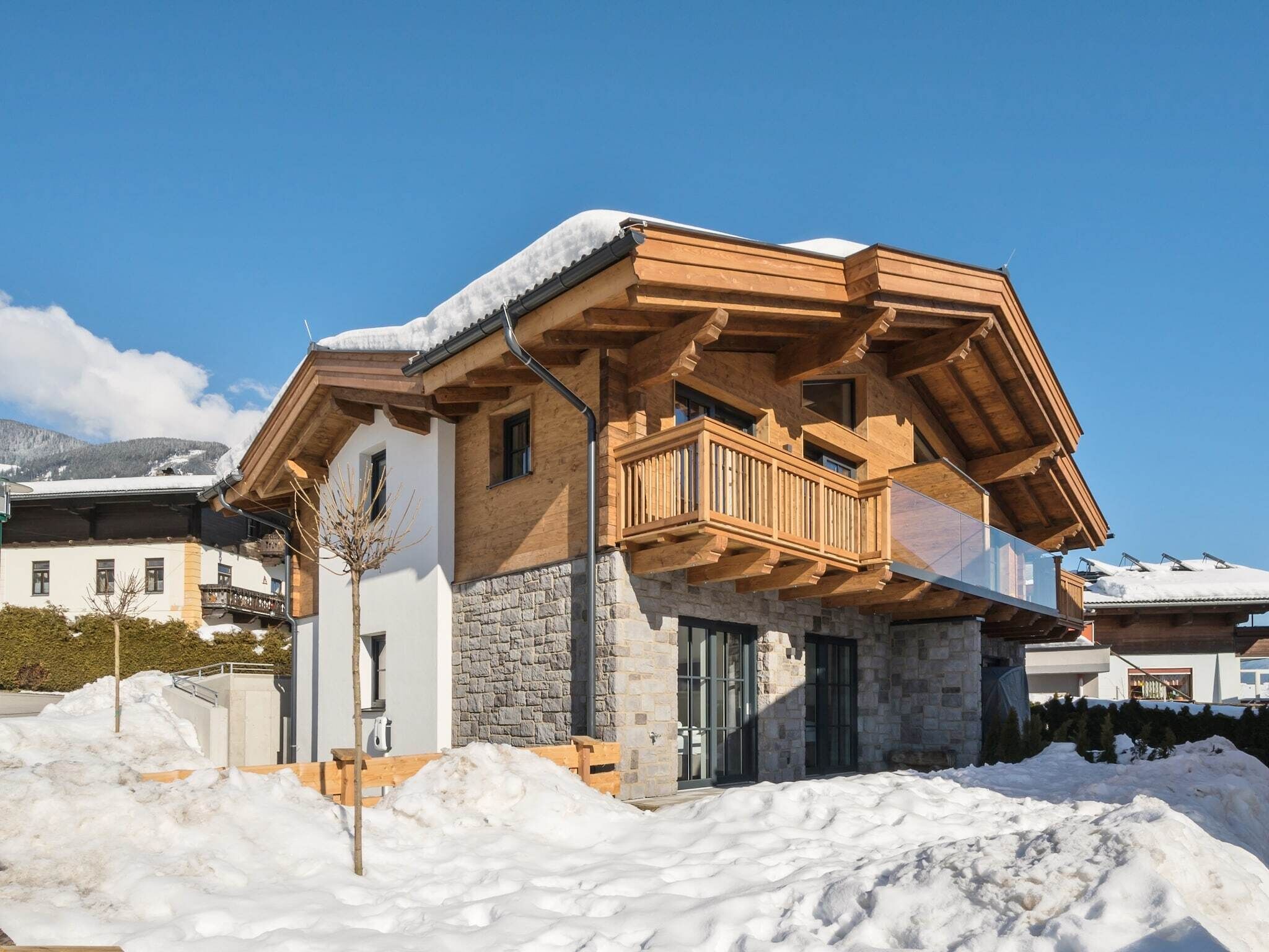 A chalet-style building with a stone facade, wooden balcony, and a snow-covered roof.