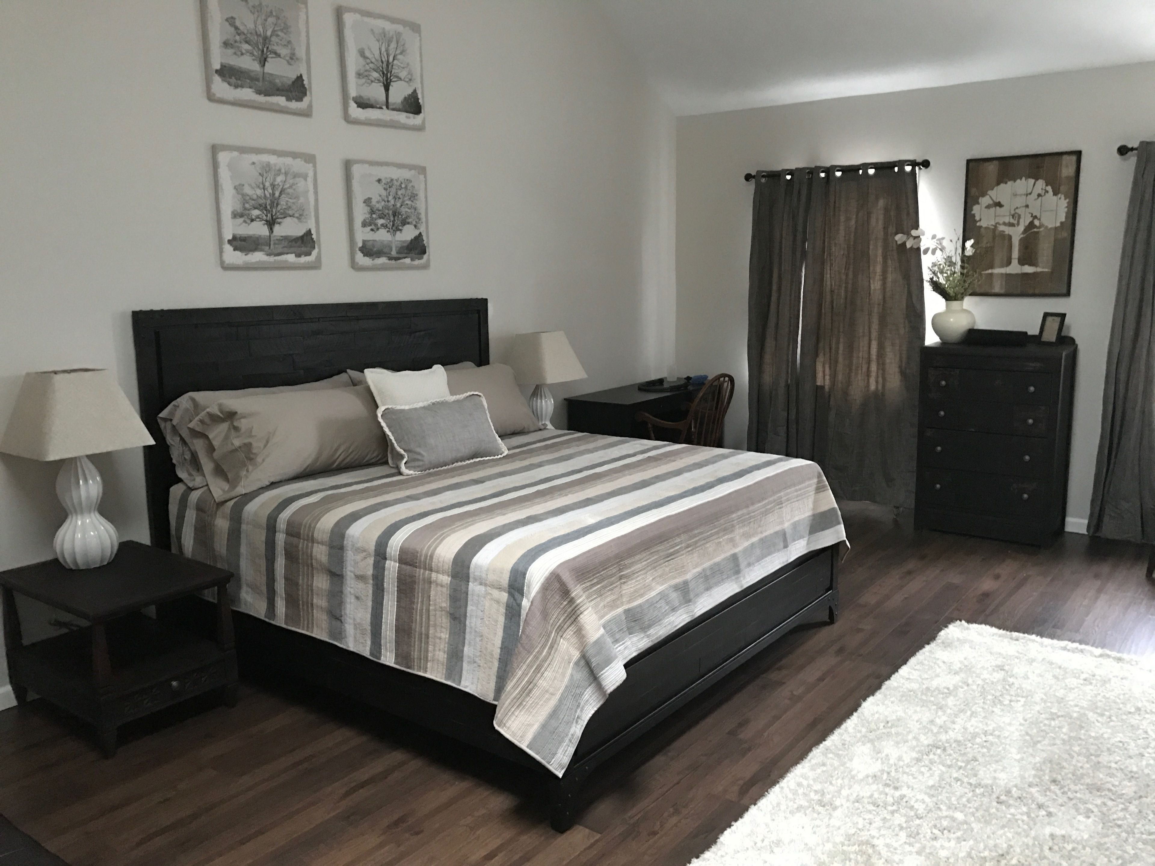 A bedroom with a large bed, two bedside tables, a dresser, and a chair. There are four framed pictures on the wall.
