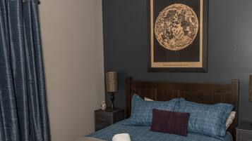 A bedroom with a bed, a ceiling fan, a nightstand, a lamp, and a framed artwork on the wall.
