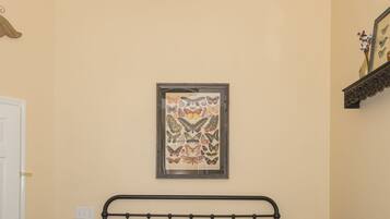 A neatly made bed with a red pillow, two bedside lamps, and a wall-mounted picture frame.