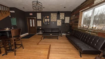 Un interior acogedor con piso de madera, un sofá de cuero negro, una mesa de comedor con sillas y una escalera.