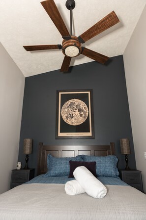 A bedroom with a bed, a ceiling fan, a framed artwork, and bedside lamps.