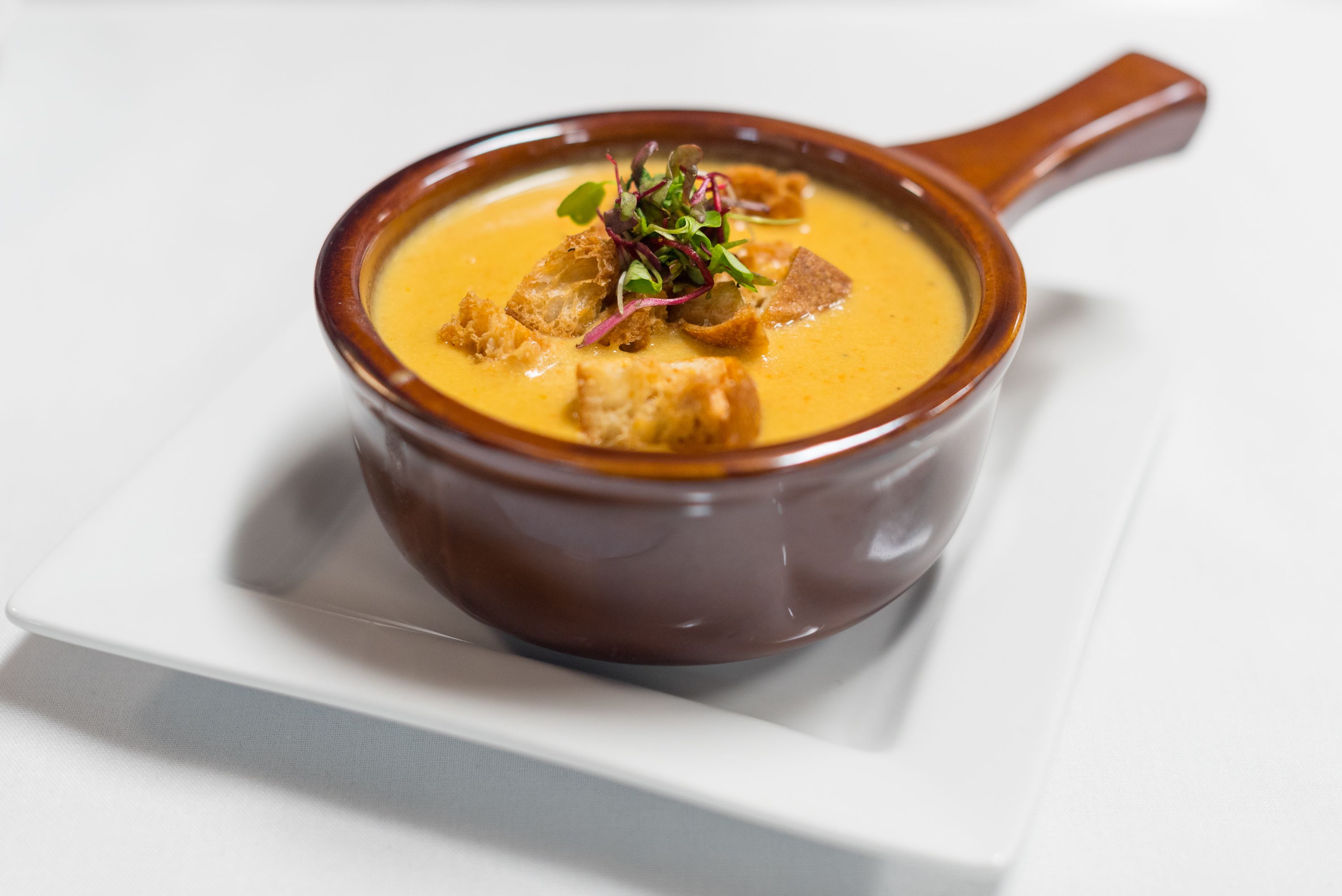 Un tazón de sopa con crutones y vegetales verdes sobre un plato blanco.