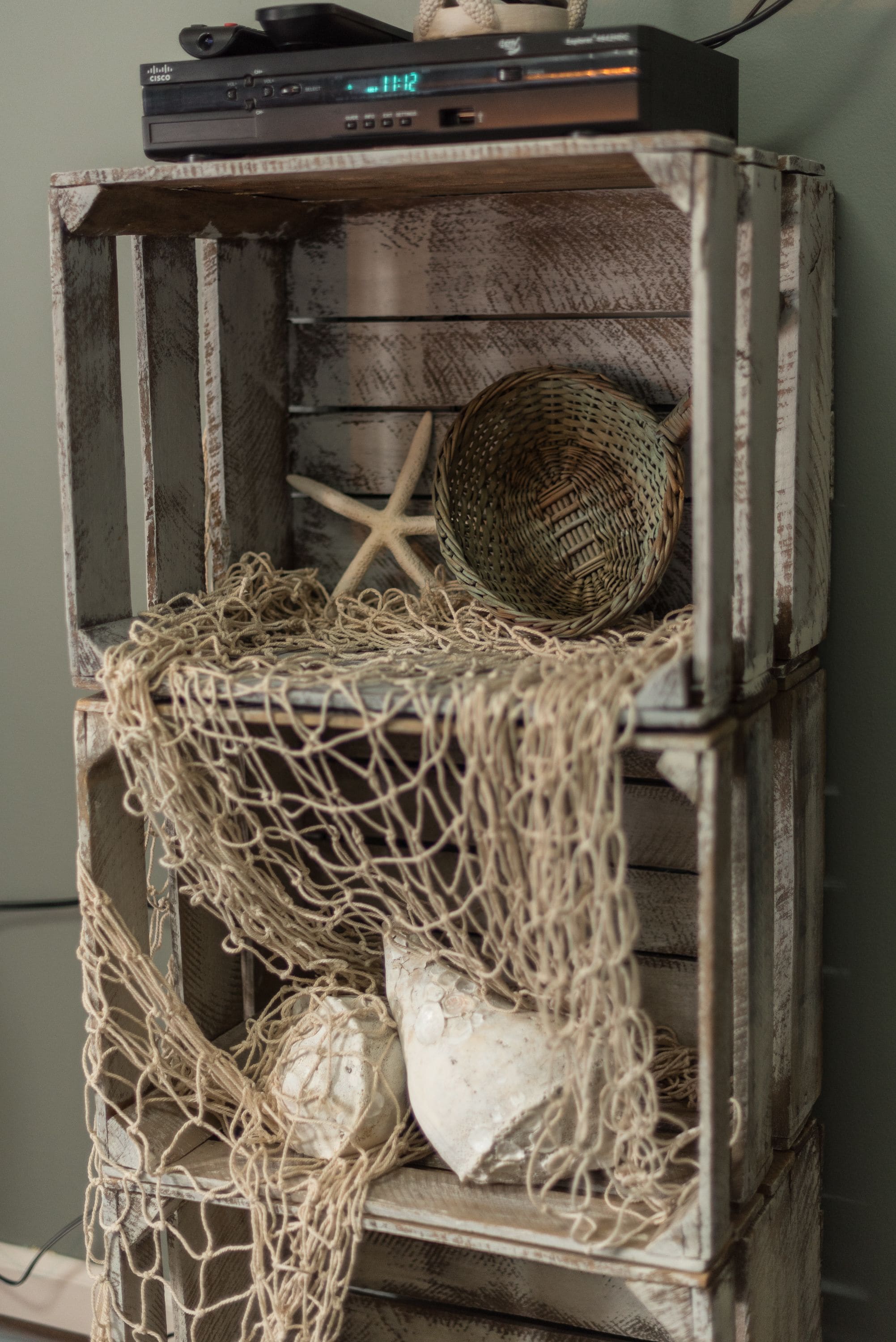 A rustic wooden shelf with a starfish, a woven basket, and a white object.