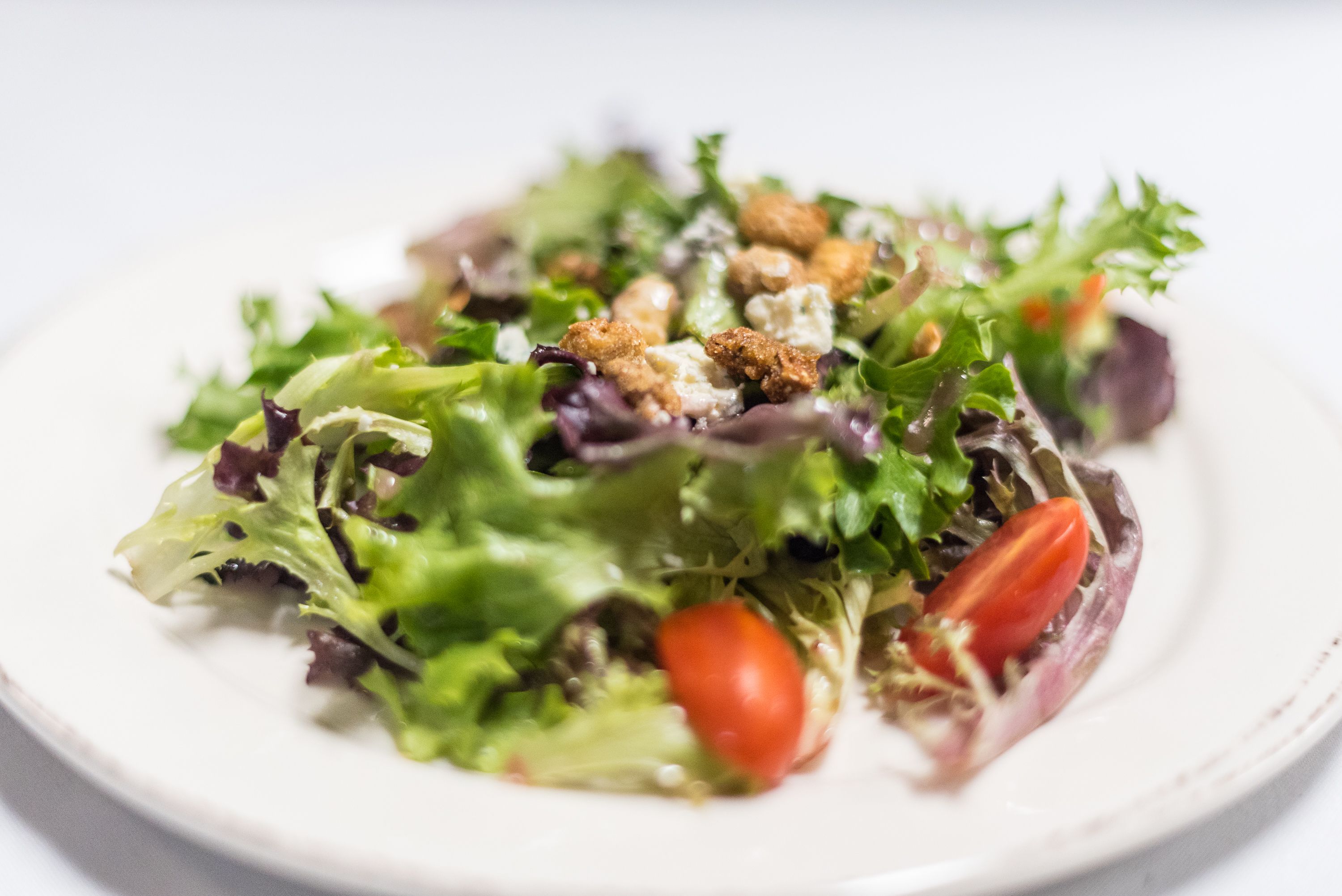 A plate of mixed greens salad with croutons and a cherry tomato.