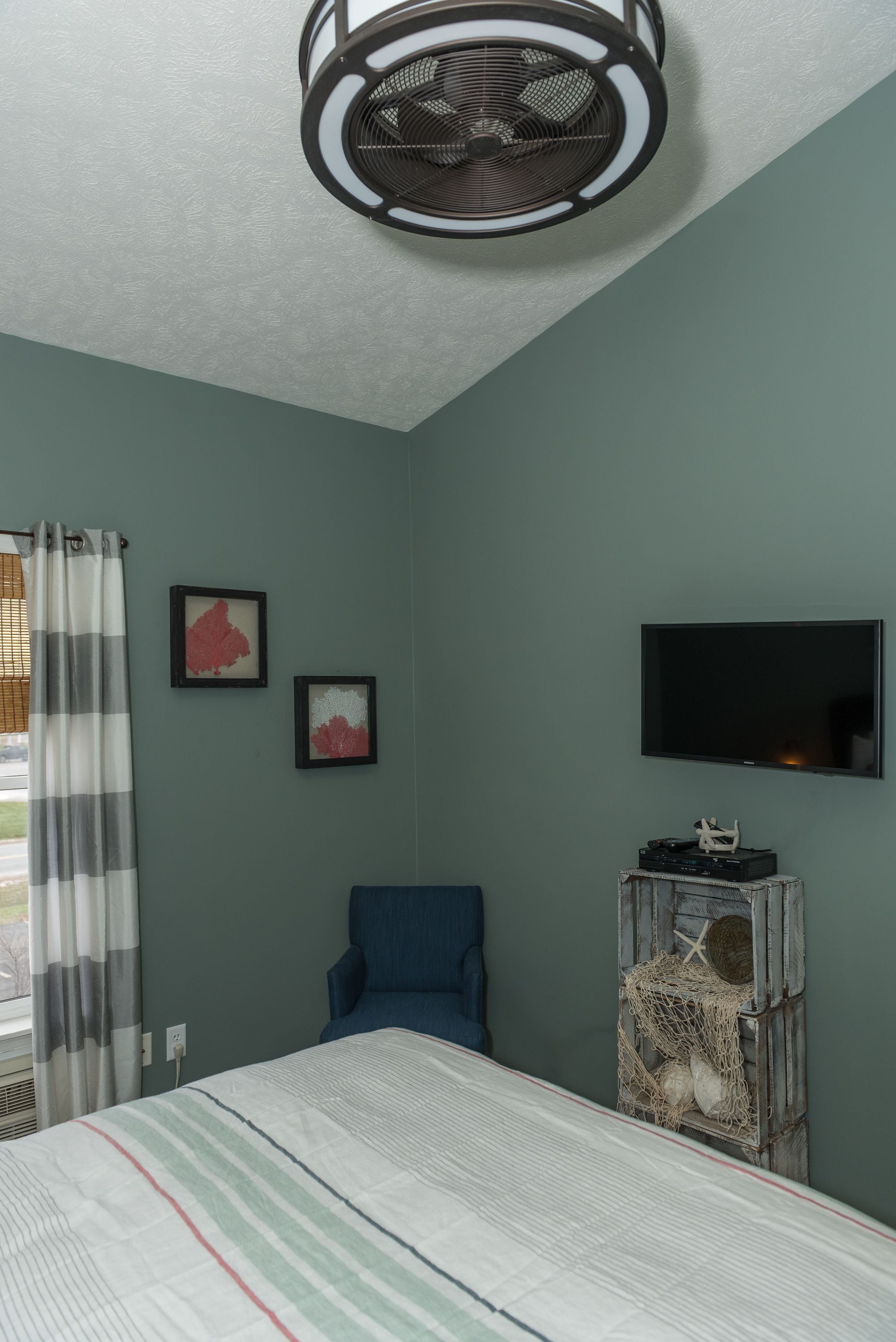 Ein Schlafzimmer mit Bett, Deckenventilator, Fernseher und einem Fenster mit Vorhängen.
