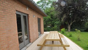 A brick building with a patio area featuring a wooden picnic table. - Holiday Home in Marche-en-Famenne near Train (Marloie)