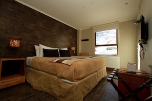 Une chambre avec un grand lit, une tête de lit en bois, une fenêtre avec vue, une télévision et un bureau avec une chaise.