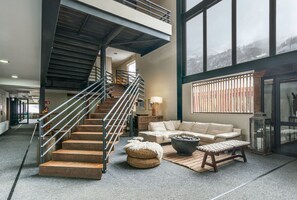 A spacious living area with a staircase, a sofa, a coffee table, and a large window with a view of a snowy landscape. - Hotel Alto Nevados (Pinto)