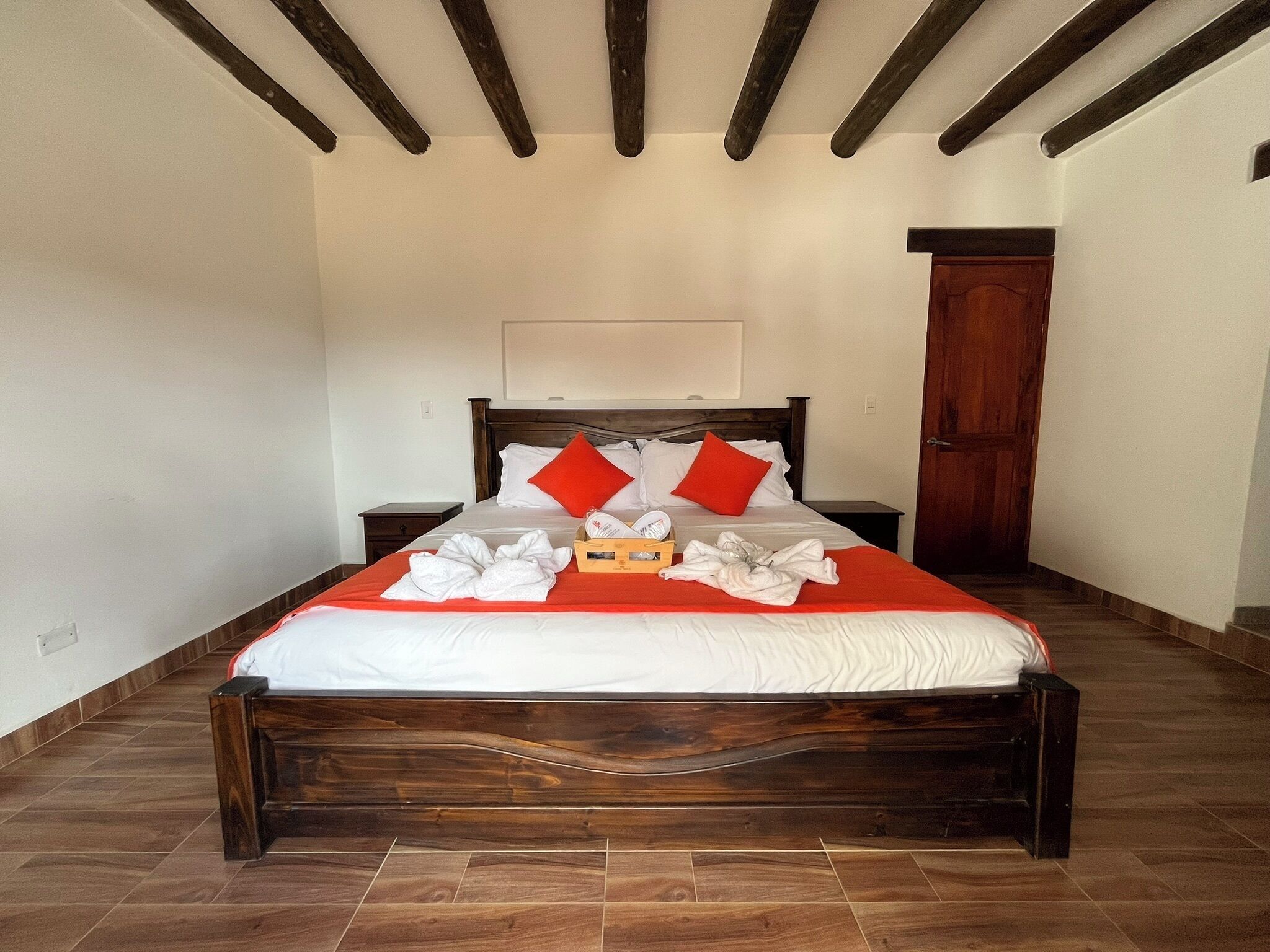 Una cama bien hecha con sábanas blancas y almohadas rojas, cabecera de madera y suelo de madera.