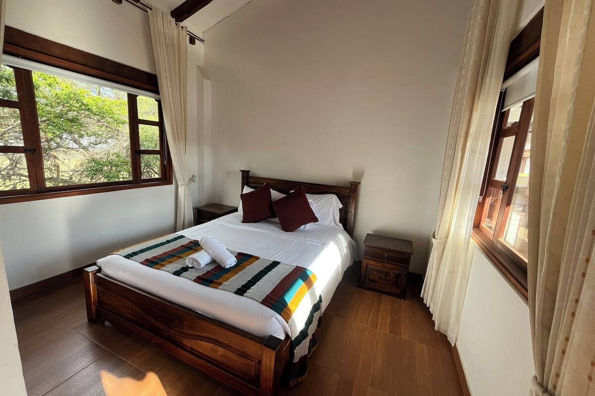 A bedroom with a wooden bed, white bedding, and a view of greenery outside.