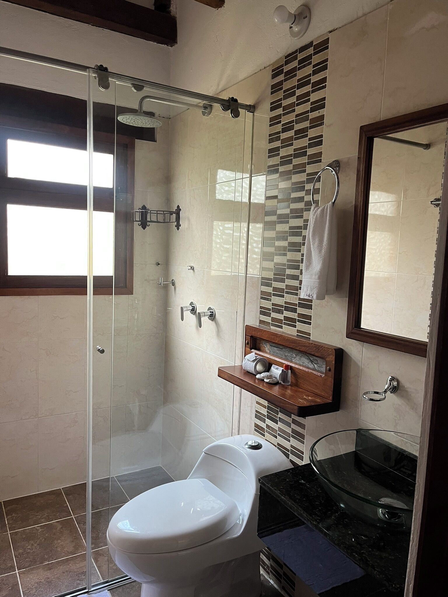 Une salle de bain moderne dotée d’une douche à parois de verre, de toilettes, d’un lavabo avec un vasque en verre et d’un meuble-lavabo avec un miroir.