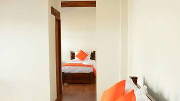 A hotel room with a wooden ceiling, a bed with white and orange bedding, and a wooden headboard.