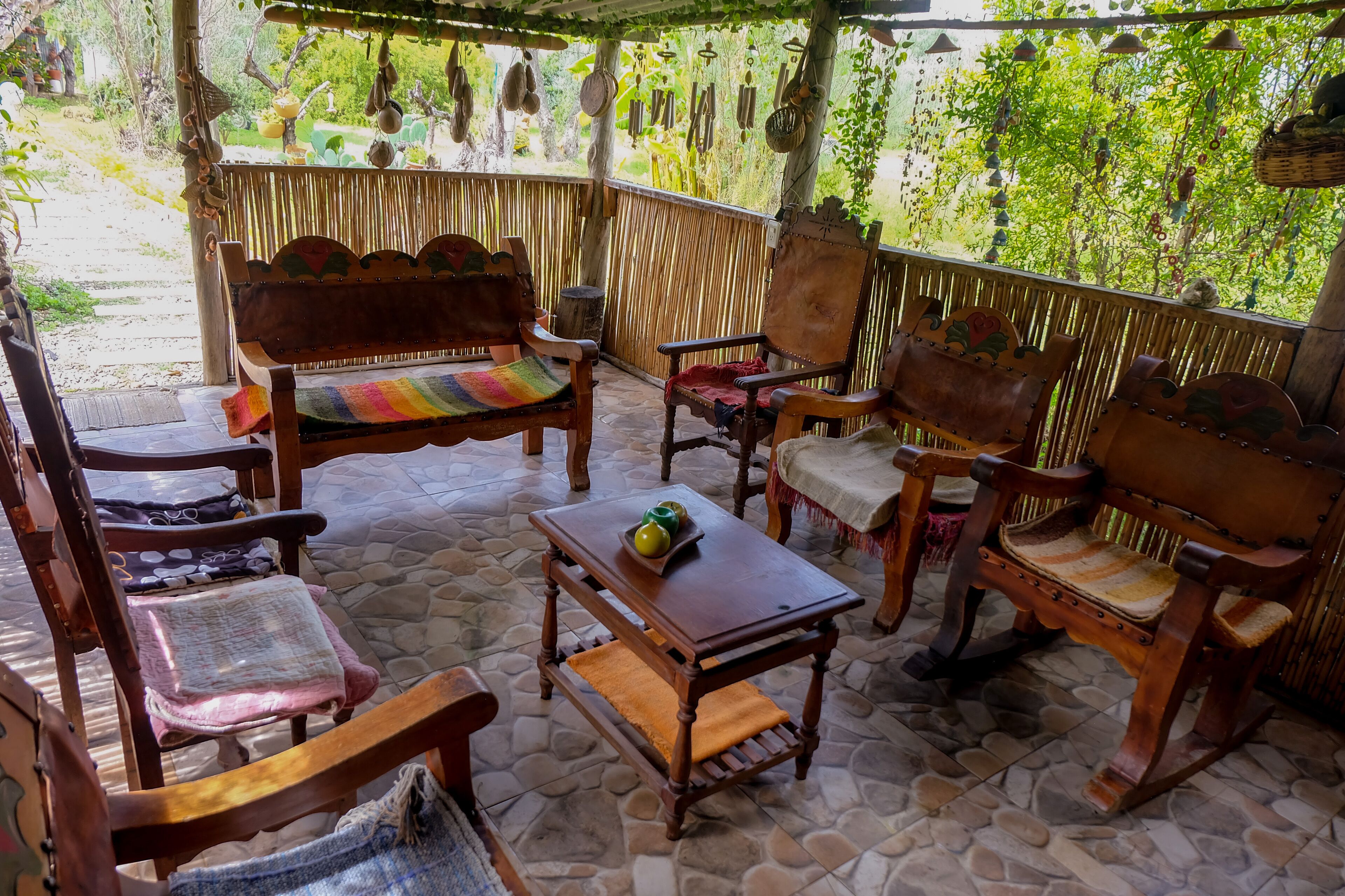 A covered outdoor seating area with wooden furniture and a stone floor.