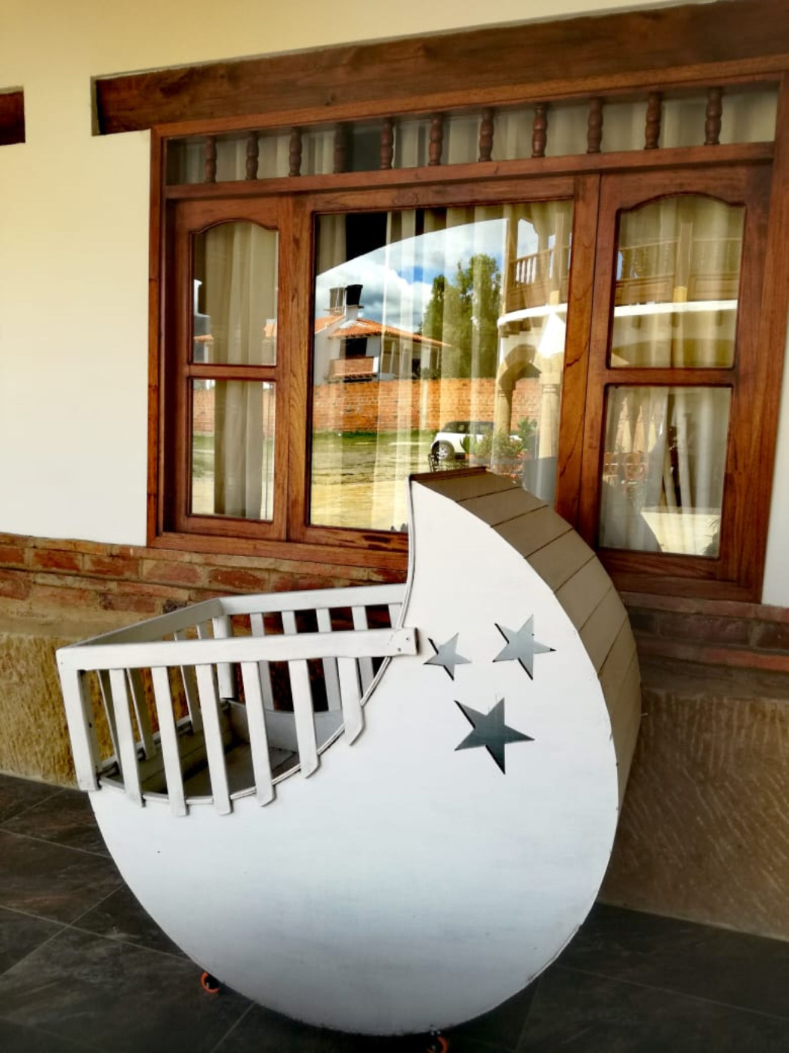 Zona de juegos en forma de media luna blanca, con barandilla blanca y tres estrellas pintadas, ubicada frente a una ventana con marcos de madera y cortinas.