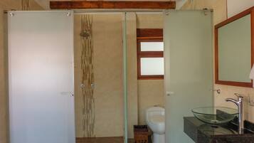 Un baño con cabina de ducha de vidrio, inodoro, lavabo de vidrio y viga de techo de madera.