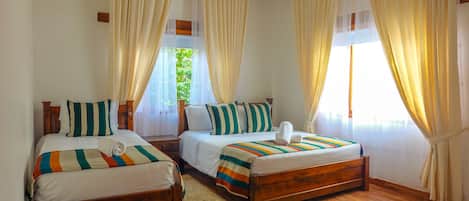 Una habitación de hotel con dos camas de madera, cada una con ropa de cama y almohadas a rayas, un mesita de noche de madera y suelo de madera.