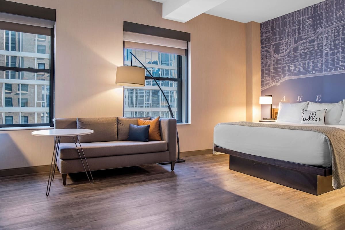 Une chambre d’hôtel avec un lit, un canapé, une petite table et une grande fenêtre.