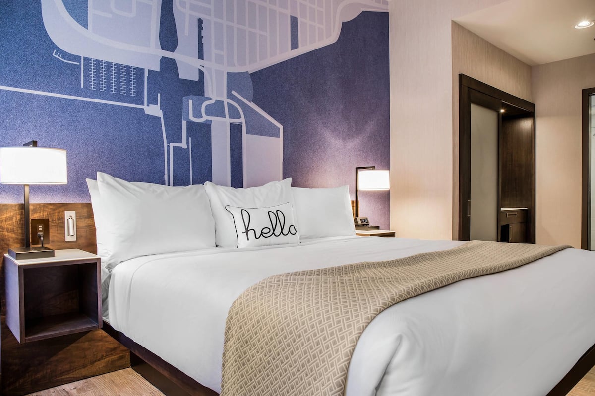 Une chambre d’hôtel avec un grand lit, deux tables de chevet avec des lampes, une fresque murale et une porte.