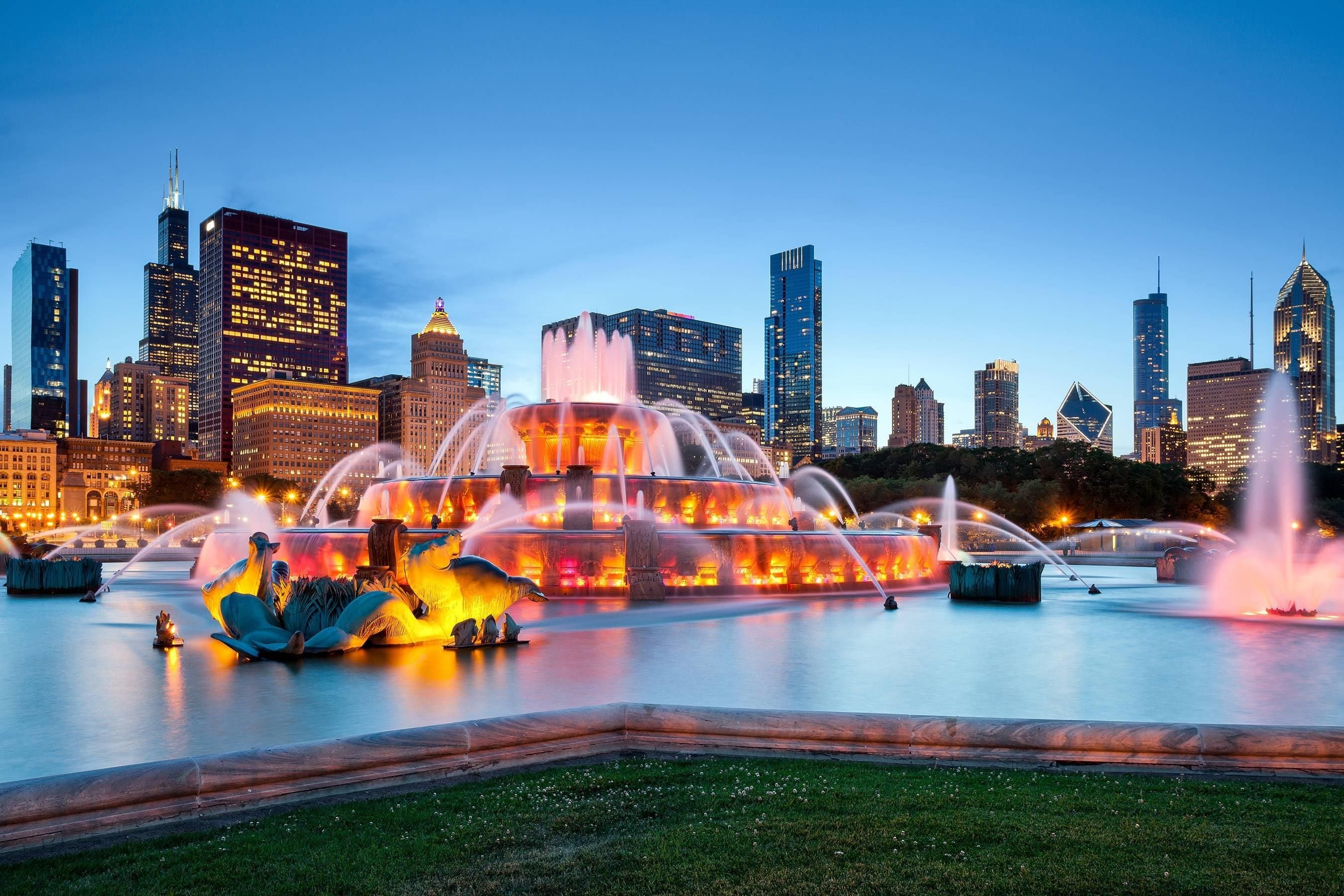 A cityscape with a prominent fountain in the foreground and a skyline of modern buildings in the background.