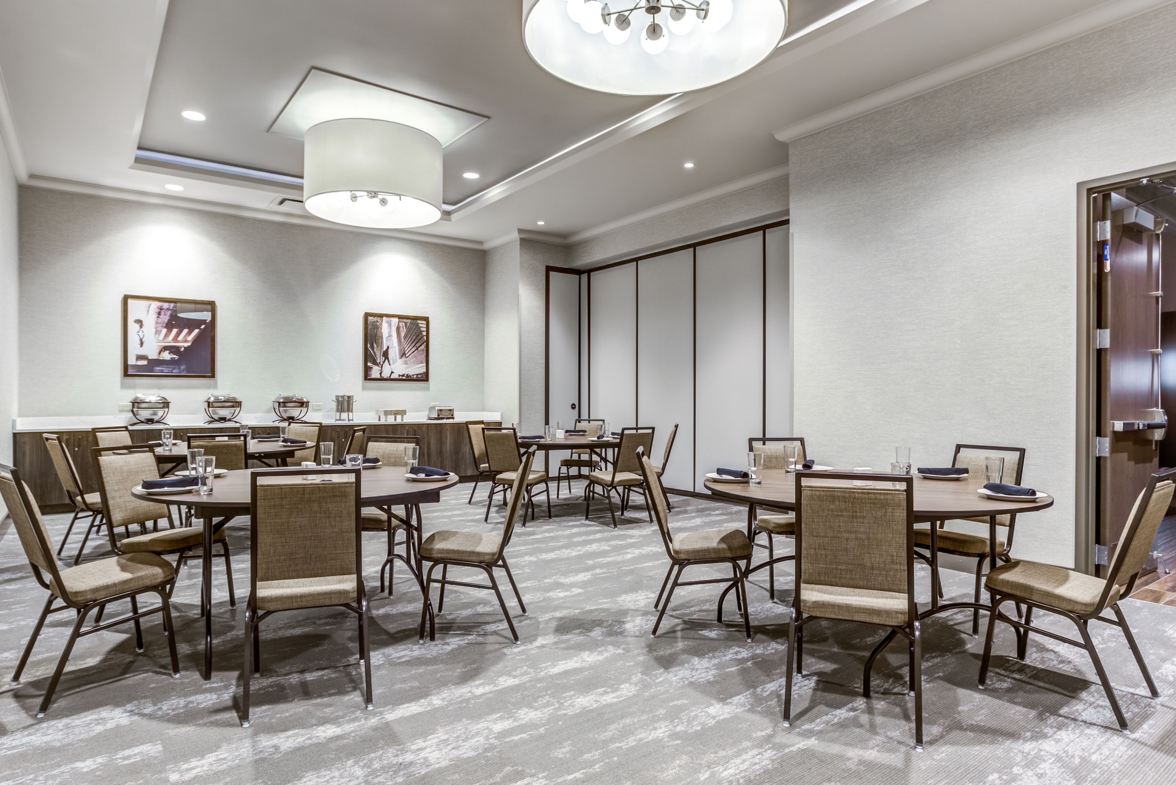 Une salle de conférence avec des tables et des chaises rondes, un grand lustre et des œuvres d’art encadrées accrochées aux murs.