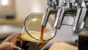 A hand holding a glass receiving a beverage from a tap.