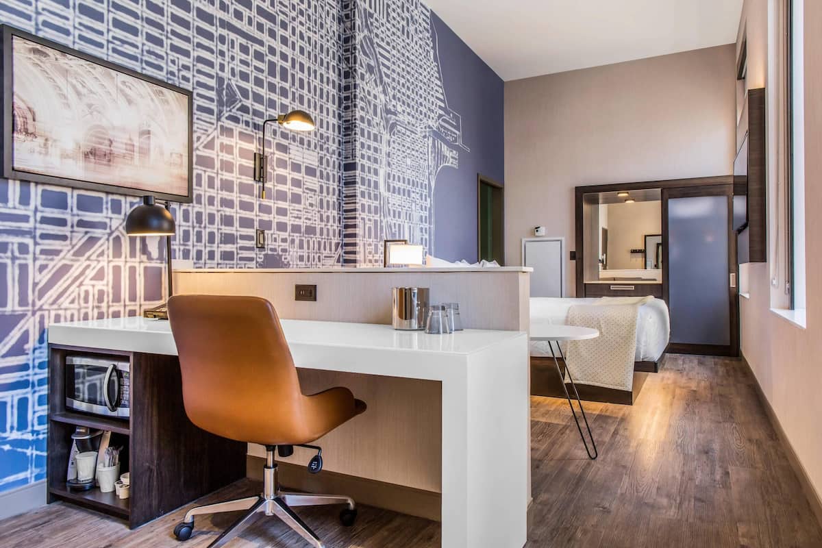 Une chambre d’hôtel moderne avec un bureau blanc, un fauteuil en cuir marron et un grand miroir.